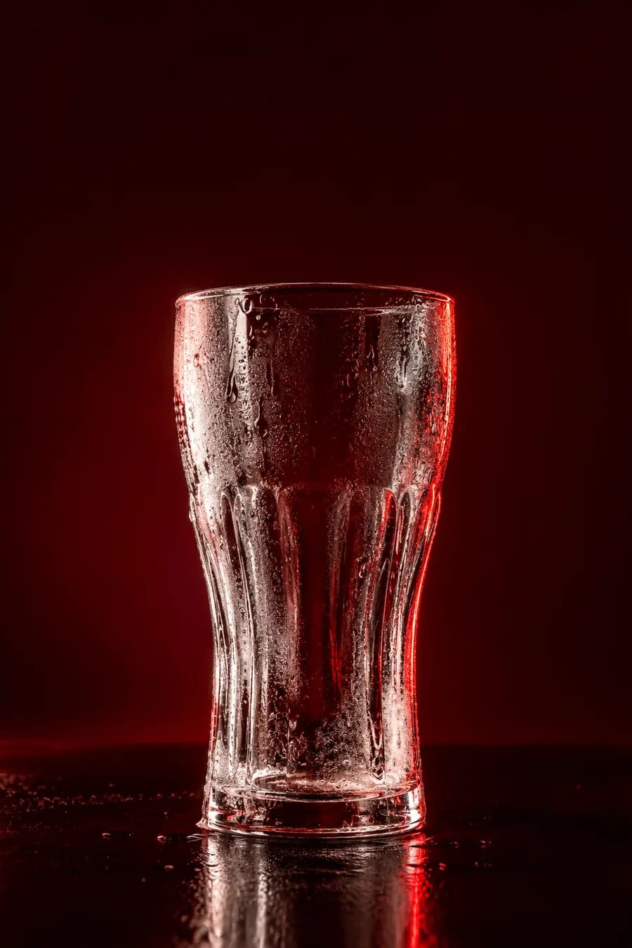 Bicchiere Coca-Cola alto e vuoto, appannato dal freddo, su fondo rosso scuro